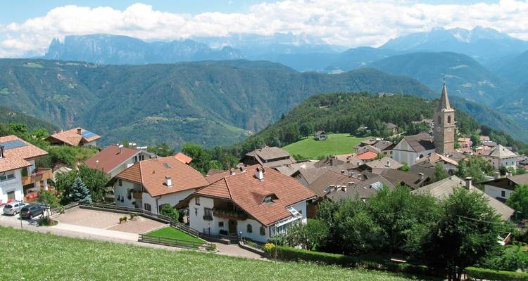 Village nestled in the hills with a church and distant mountains.