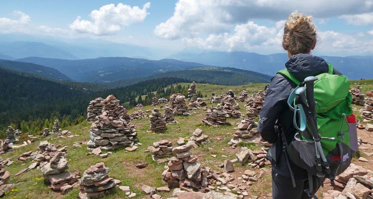 Hiker walking through a field of cairns with mountainous backdrop.