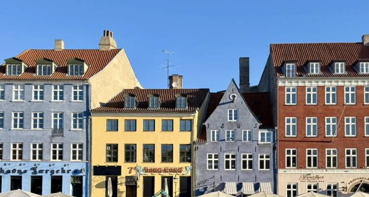 Row of colorful historic townhouses under a clear blue sky in Copenhagen’s Nyhavn district.