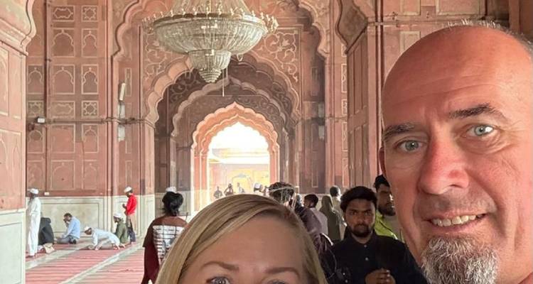 Selfie de deux voyageurs à l'intérieur d'une arcade ornée de mosquée en grès rouge avec d'autres visiteurs en arrière-plan.