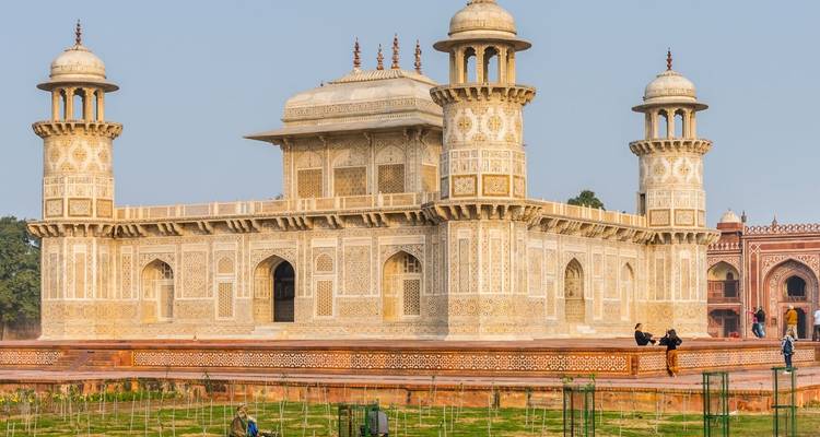 Le tombeau d'Itimad-ud-Daulah finement sculpté brillant au soleil avec une paire de visiteurs à proximité.