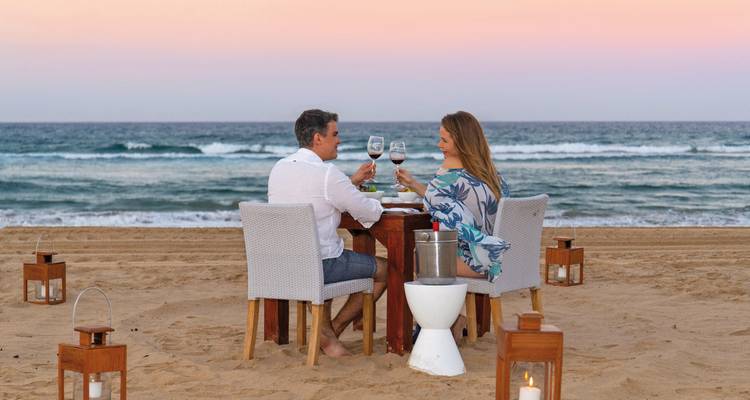 Dîner romantique au bord de la plage avec un couple qui trinque au coucher du soleil.