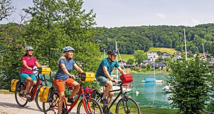 Cyclistes roulant le long d'un lac avec des bateaux et des maisons à proximité.