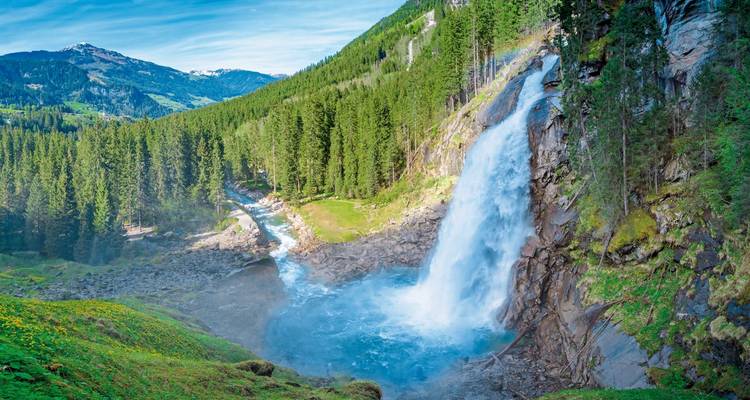 Haute cascade entourée d'une forêt verdoyante et de montagnes.