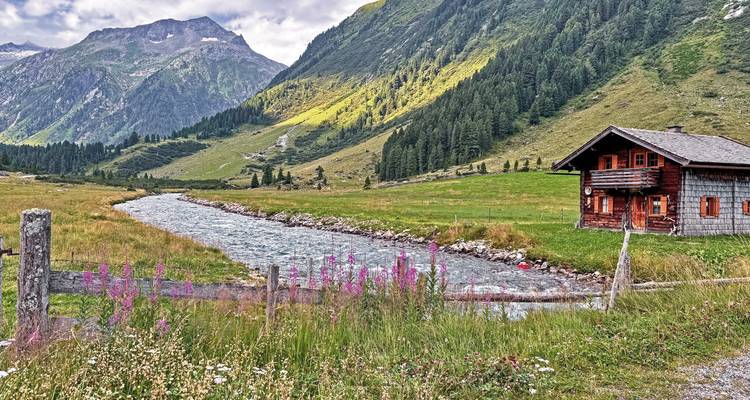 Valle de montaña con un río y una casa de madera.