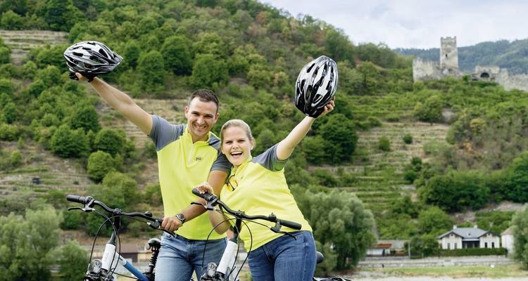 Glückliche Radfahrer posieren mit Helmen in einer hügeligen Weinberglandschaft.