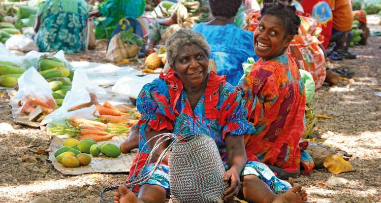 Frauen sitzen auf einem Markt mit tropischen Früchten.