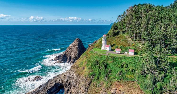 Lighthouse perched on a rugged cliff with dense forest on coast.