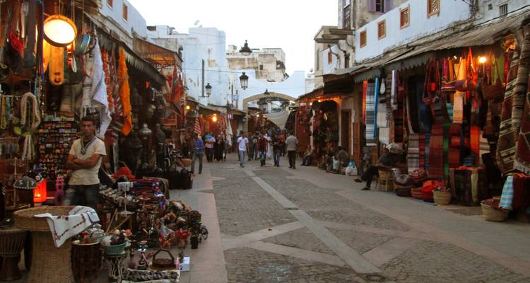 Marktszene mit bunten Waren und Dekorationen, die in einer schmalen, von Ständen gesäumten Straße ausgestellt sind.