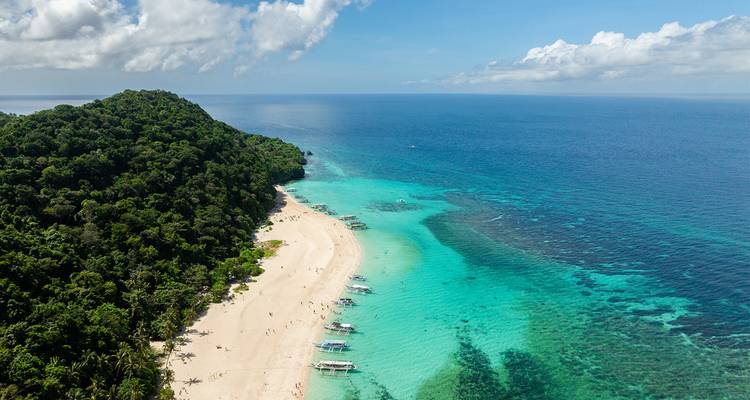 Aerial view of a curved white-sand beach fringed by rainforest and turquoise waters stretching into the ocean.