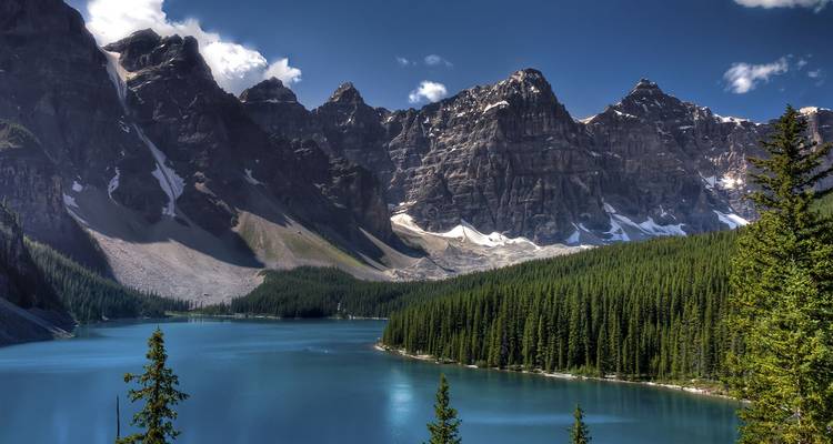 Lago Moraine color turquesa rodeado de un denso bosque de pinos con los dramáticos Diez Picos elevándose sobre ti.