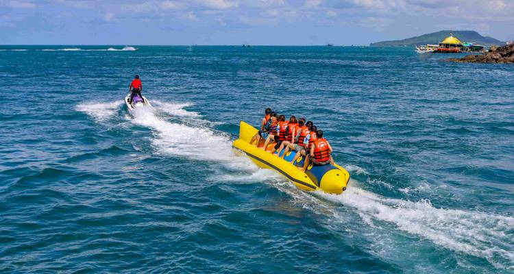 Een jetski trekt een bananenboot vol lachende passagiers over blauw oceaanwater.