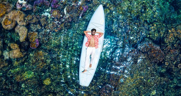 Luchtfoto van een man die ontspant op een paddleboard boven kristalhelder water met koraalrif.