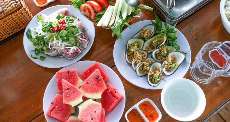 Bovenaanzicht van een Vietnamees gerecht met zeevruchten, salade en gesneden watermeloen op een houten tafel.