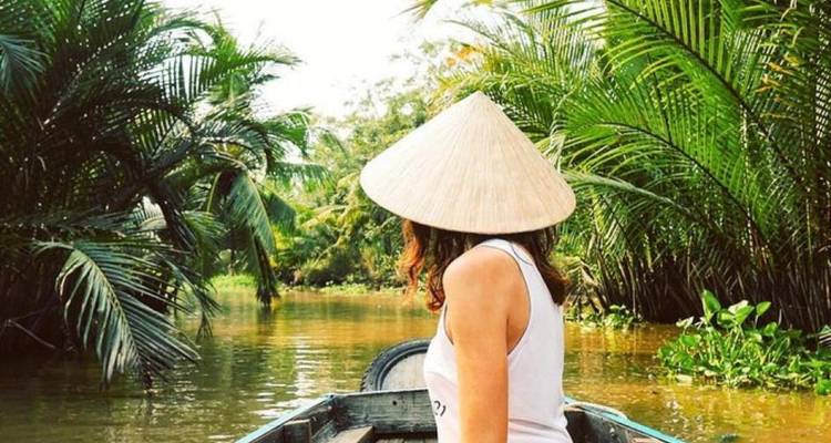 Frau mit traditionellem Hut in einem Boot auf einem üppigen Kanal