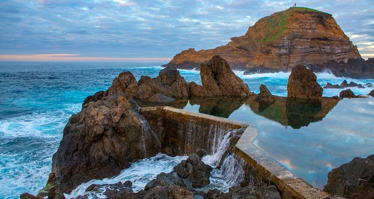 Felsige Küstenlandschaft mit tosenden Wellen unter dramatischem Himmel.
