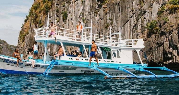 Tourists enjoy a boat excursion beside towering limestone cliffs and turquoise waters in El Nido.