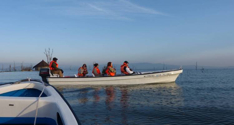 Tourists wearing lifejackets ride a small motorboat across a calm lake under a clear morning sky.