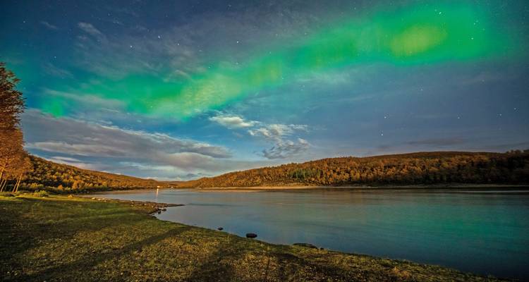 Northern lights over a calm river under a starry sky.