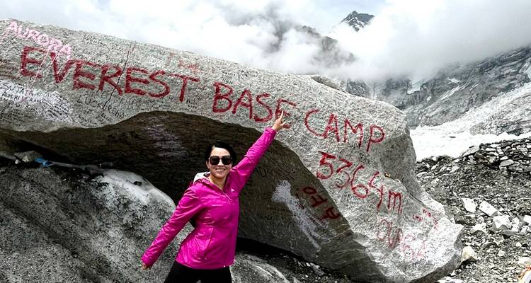 Person zeigt auf die Aufschrift 'Everest Base Camp' auf einem Felsen.