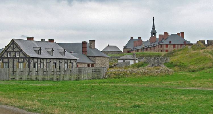 Los edificios y murallas de la Fortaleza Histórica de Louisbourg se encuentran en un terreno ondulado y cubierto de pasto bajo un cielo nublado.