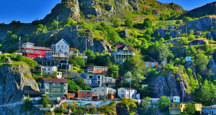 Casas coloridas pegadas al acantilado anidadas en una ladera rocosa cubierta de vegetación bajo un cielo azul brillante.