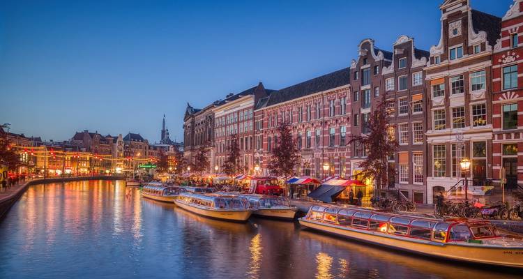 Canal illuminé avec bâtiments traditionnels et bateaux le soir.