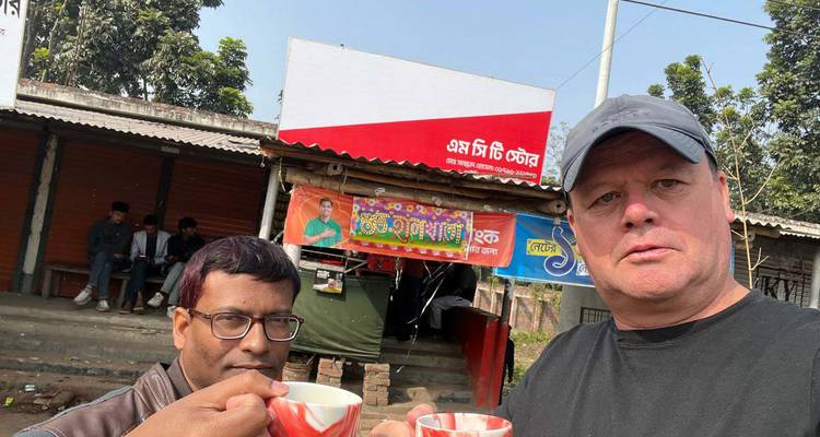 Two men hold clay cups of tea for a roadside selfie in a rural Bangladeshi town.