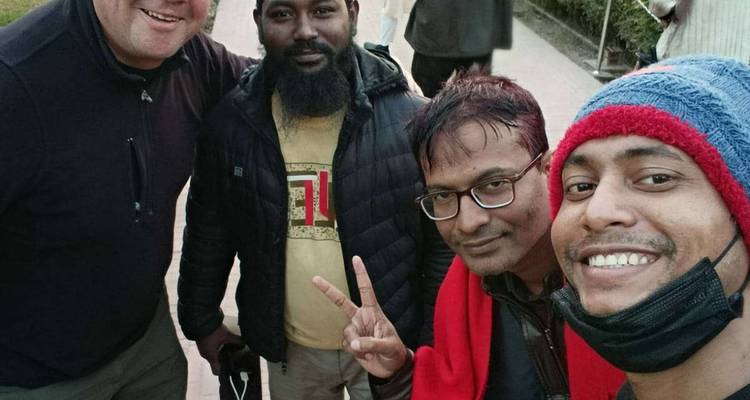 Four travelers smile for a close selfie, one flashing a peace sign on a busy street.