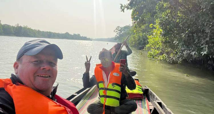 Travelers in lifejackets pose on a small river boat amid lush riverside forest.