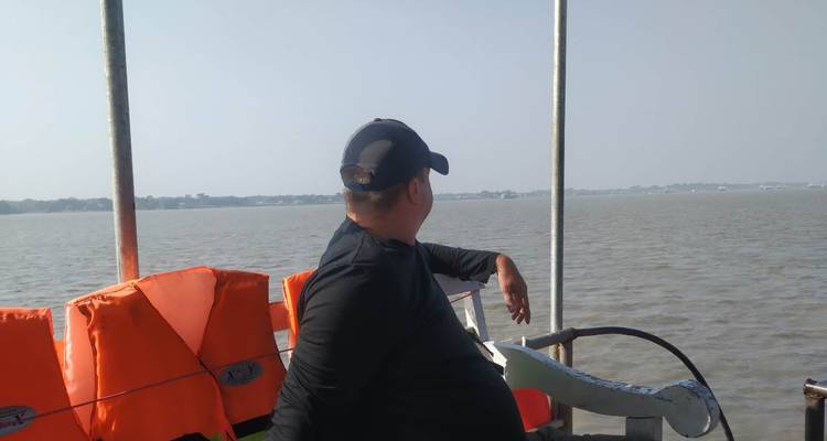 A man wearing a cap looks over open water from the side of a ferry deck.