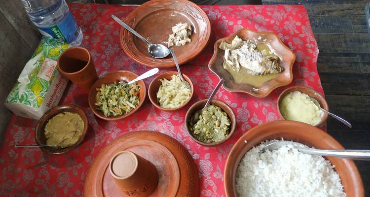 Traditional Bangladeshi meal served in terracotta bowls on a red patterned tablecloth.