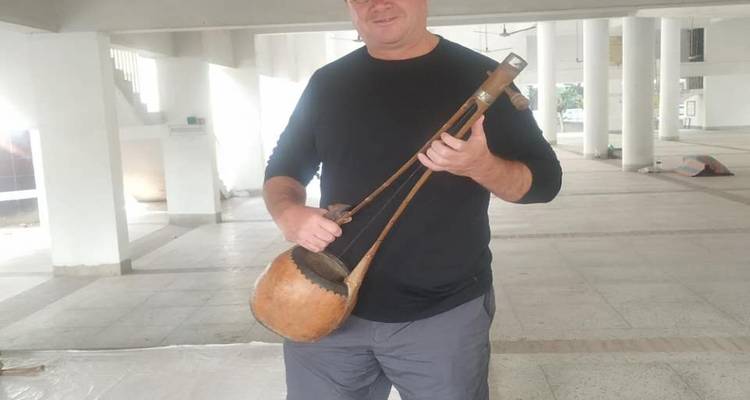 Man demonstrates a traditional string instrument inside a large open hall.