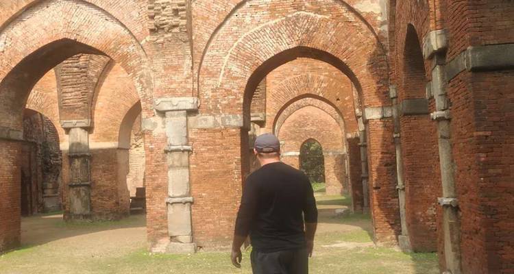 Un hombre camina a través de los arcos de ladrillo elevados de una estructura antigua y abandonada.