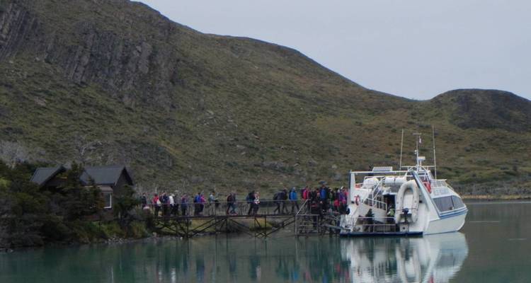 Ausflugsboot, das an einem Holzsteg an einem milchig türkisfarbenen See angedockt ist, während eine Reisegruppe inmitten von felsigen Hügeln an Bord geht