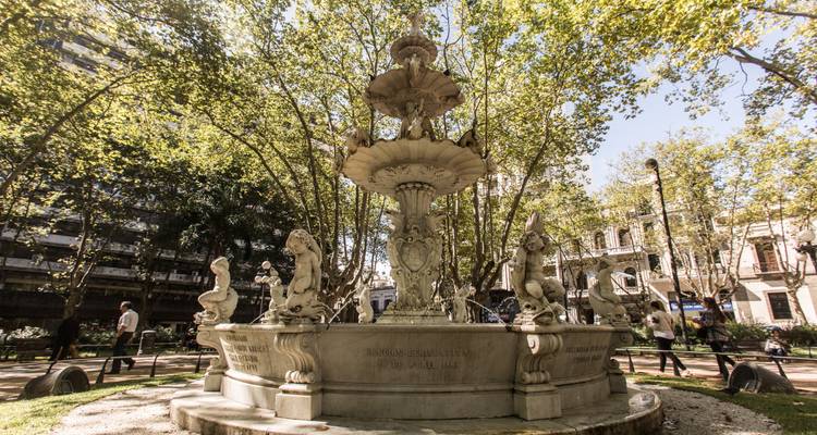 Brunnen in einem grünen Park mit vorbeigehenden Menschen.