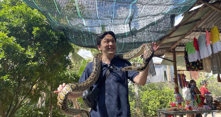 Man holding a large snake with trees in the background.