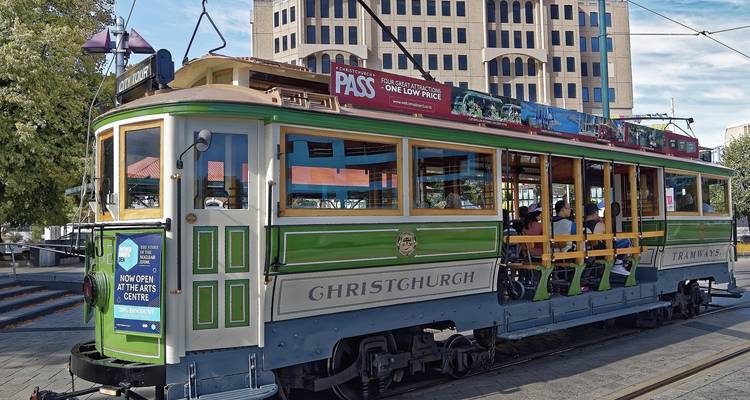 Tram vert vintage de Christchurch avec des passagers assis passant devant des bâtiments modernes de la ville