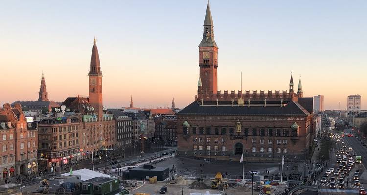 Kopenhagens stadhuis en omringende skyline bij pastelachtige zonsondergang met drukke straten eronder.