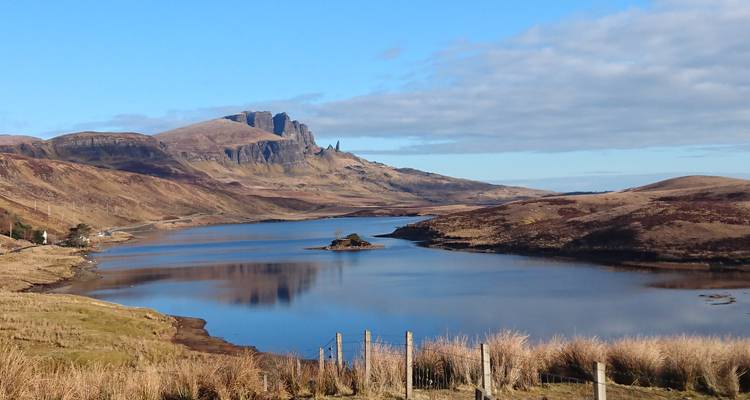 Ruhiger See, der Hügel widerspiegelt, mit der Felsnadel "Old Man of Storr" am Horizont der Insel Skye.