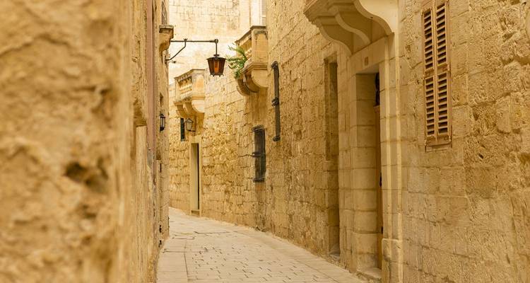 Estrecho callejón sinuoso de piedra caliza en la ciudad medieval amurallada, con cálidas paredes de piedra y ventanas con persianas.
