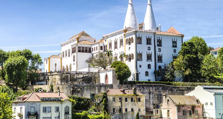 White palace with twin conical chimneys rising above a hilltop town with pastel houses