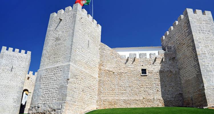 Los robustos muros de piedra y torres del Castillo de Silves ondeando la bandera portuguesa contra un cielo azul despejado