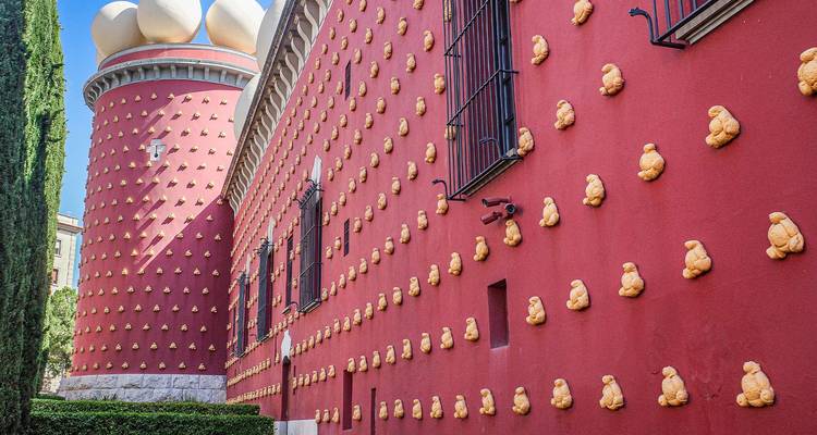 Fachada roja del Teatro-Museo Dalí decorada con ornamentos dorados y rematada con huevos gigantes, vista bajo un cielo azul despejado