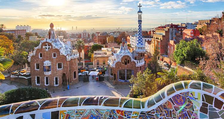 La icónica terraza de mosaico del Parque Güell con vistas a los caprichosos edificios de Gaudí y al horizonte de Barcelona al atardecer