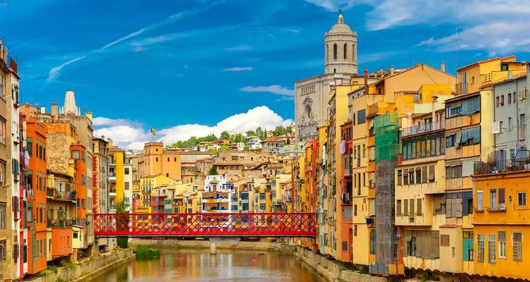 Casas coloridas junto al río y puente de hierro rojo atravesando el río Onyar en Girona bajo cielos despejados