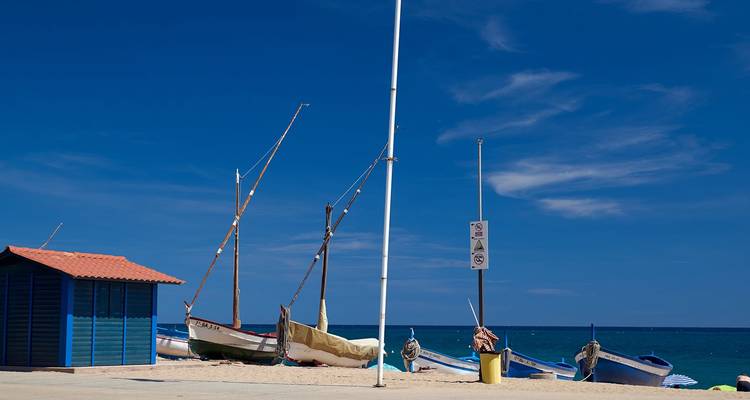 De petits bateaux de pêche reposant sur une plage méditerranéenne de sable fin sous un ciel bleu profond