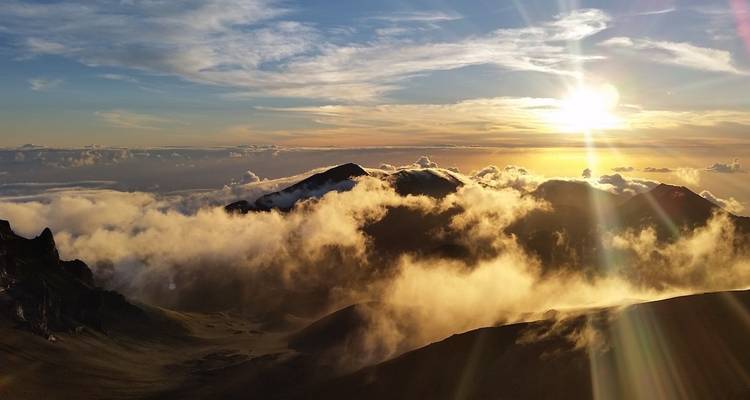 Sun setting over mountains with clouds in the foreground.