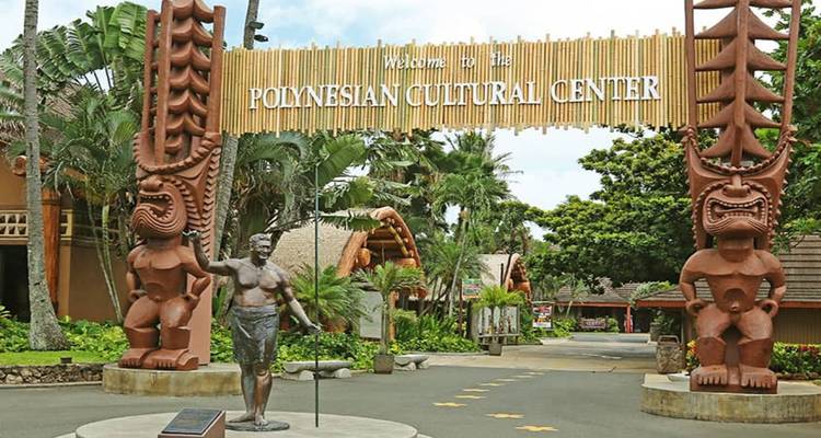 Entrance to the Polynesian Cultural Center with statues and a welcoming banner.