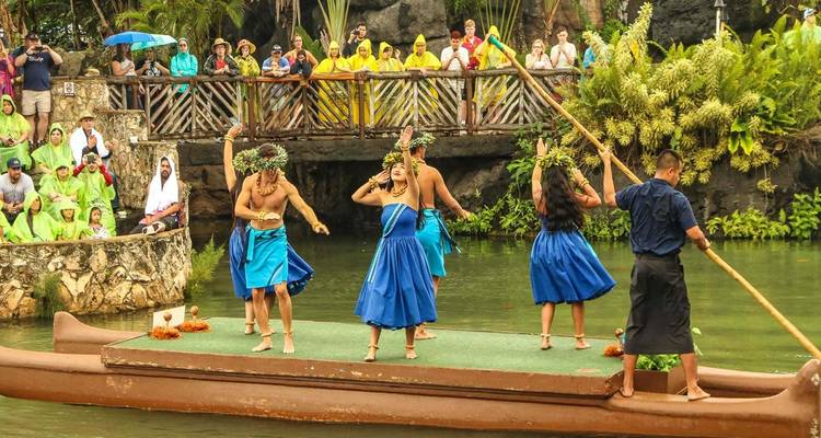 People dressed in traditional Hawaiian attire dancing on a platform on water.